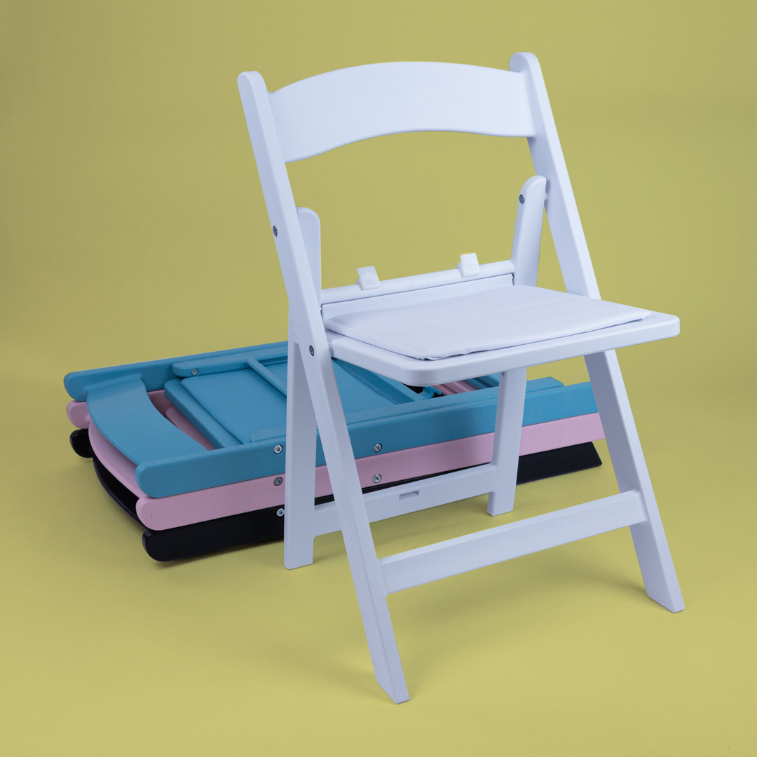 Child Size Americana Chair in white displayed upright in front of stacked pastel blue, pink, black and white mini Americana chairs on a yellow background – lightweight foldable design for kids’ events and parties.