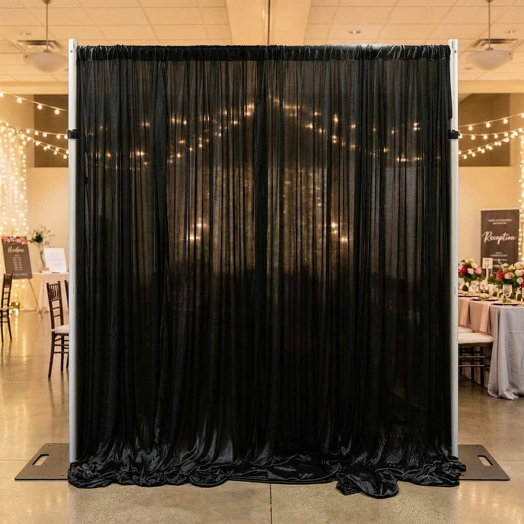 Black ice silk backdrop curtain on a backdrop stand beside a gift table with florals and fairy lights