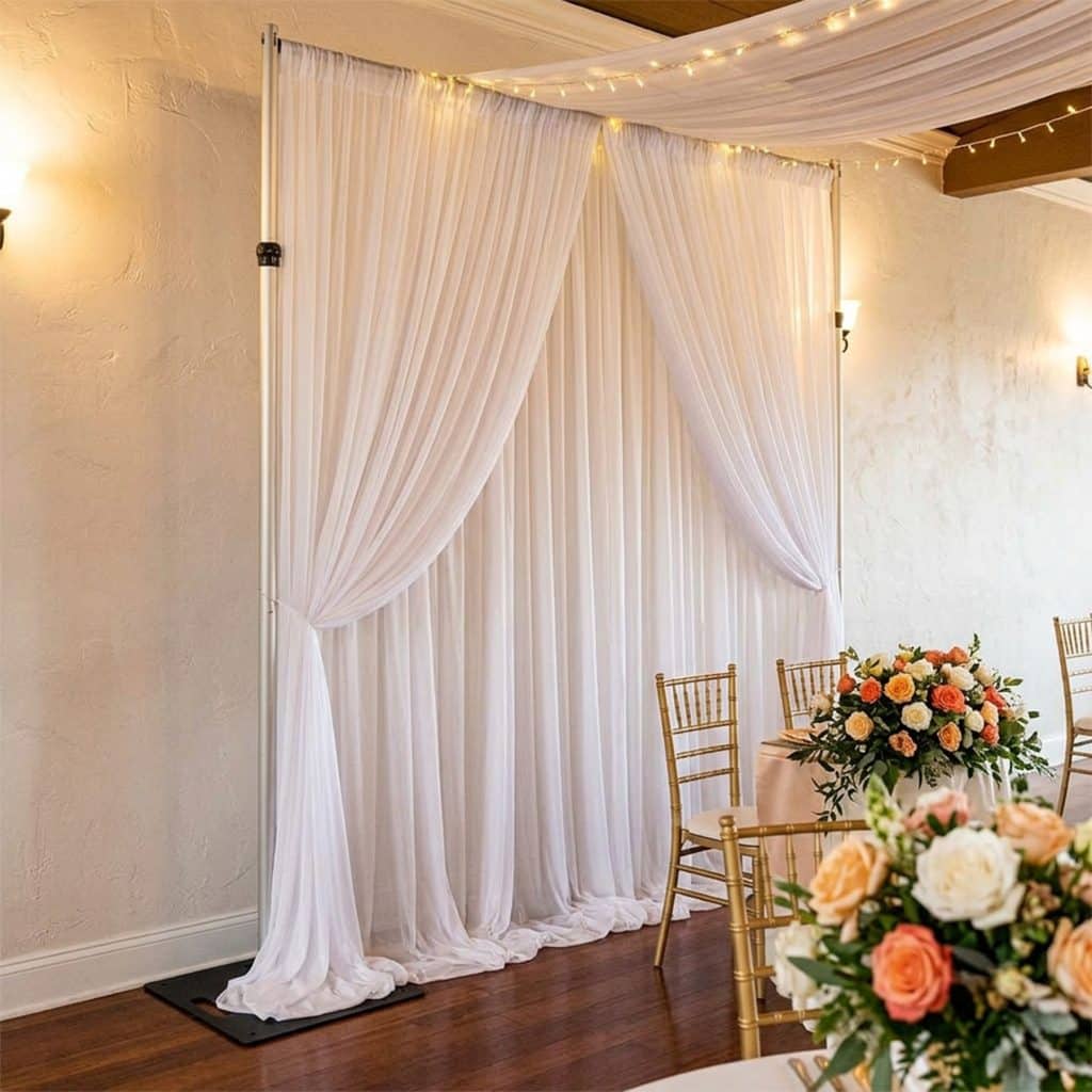 Layered white ice silk backdrop curtains tied back on a backdrop stand at a wedding reception with fairy lights