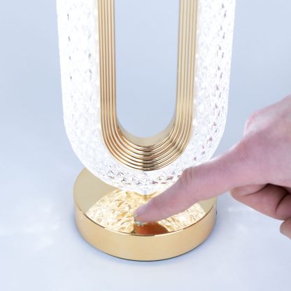 Finger touching the dimmable LED touch control on the gold base of the crystal table lamp